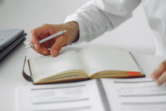 Close-up of a businessman writing notes in a diary at a modern office desk.